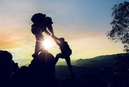 One person pulling up another person on a mountain.