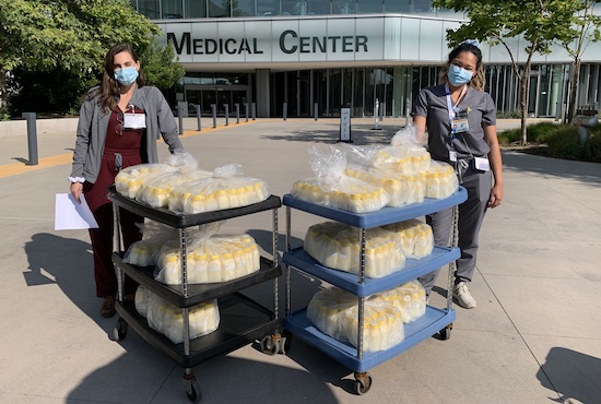 Two milk technicians standing left and right of carts with frozen donor human milk