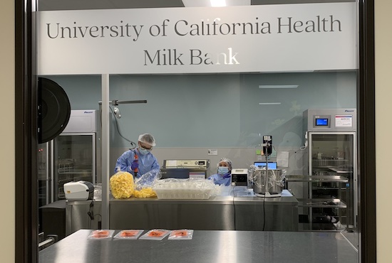 View through a window into the operating human milk bank with two people processing human milk.